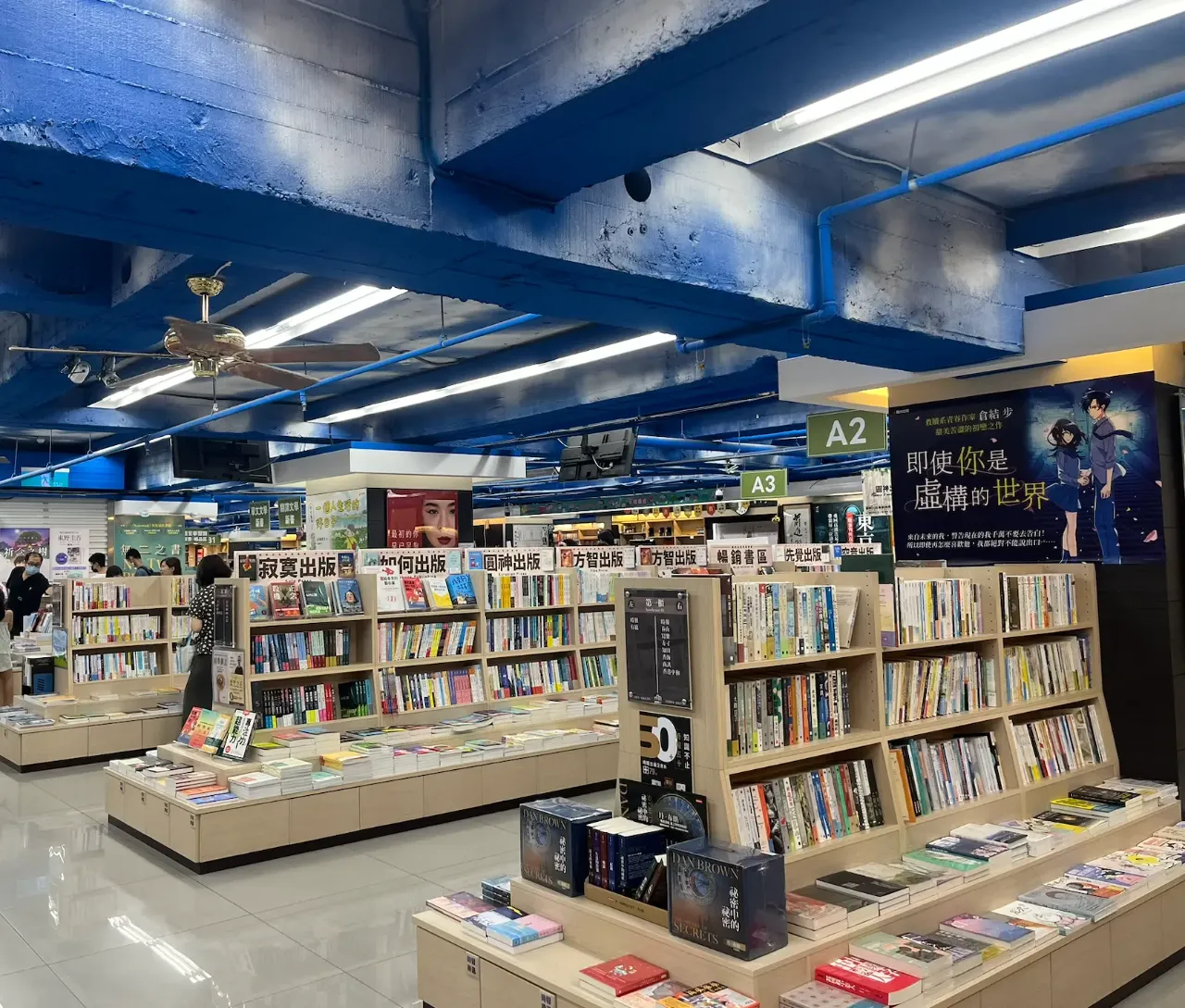 地下室書城,藍色樑柱與吊扇,架上滿是書,掛著A2、A3指示牌。
