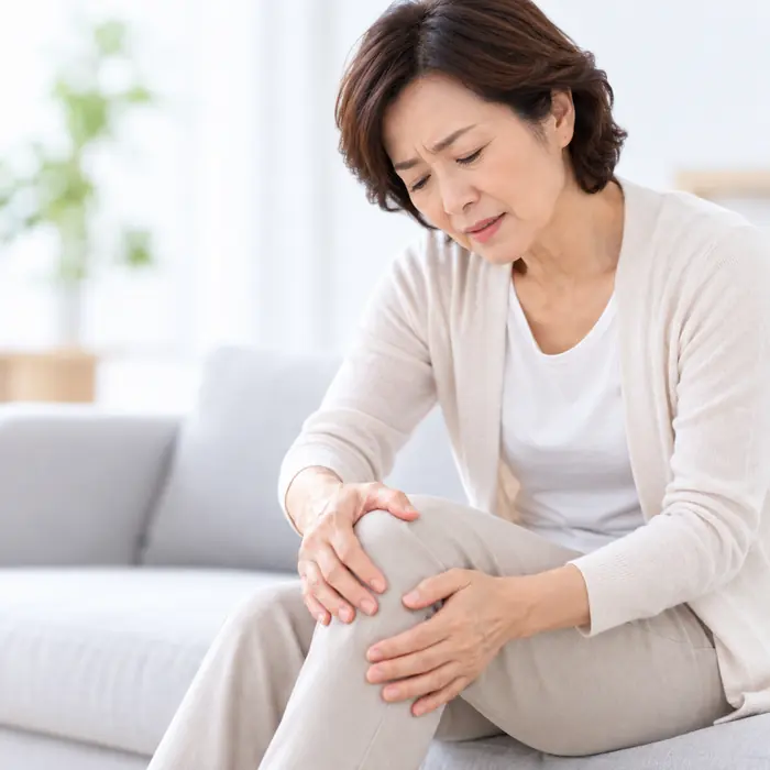女性坐在沙發上按著膝蓋
